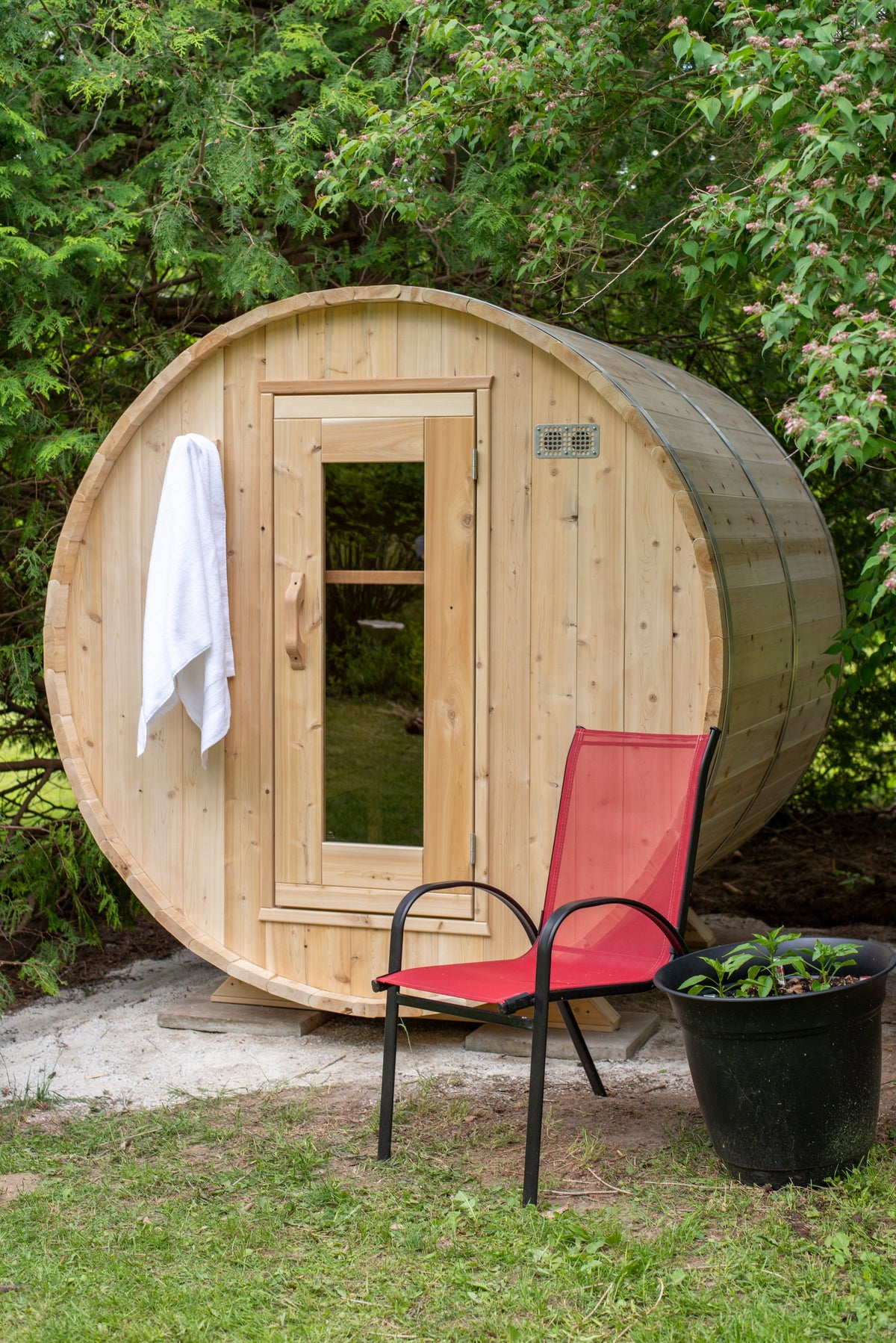 CT Harmony barrel sauna installed on a lawn with a red patio chair and planter in the foreground