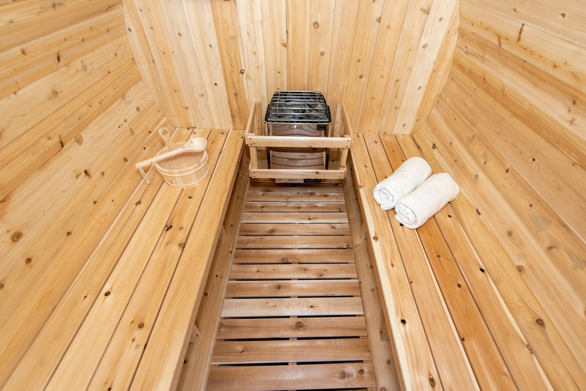 CT Harmony barrel sauna interior from the upper bench showing the heater, cedar bucket and ladle and rolled towels