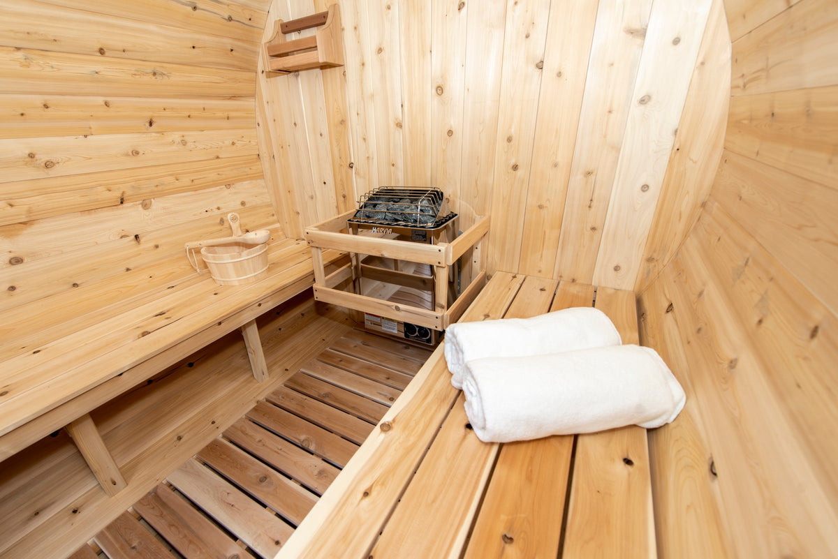 CT Harmony barrel sauna interior corner view with the electric heater on its guard rail and folded white towels on the bench