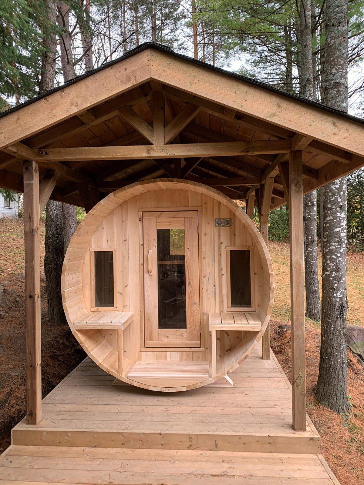 CT Tranquility barrel sauna installed under a timber pavilion in a wooded setting
